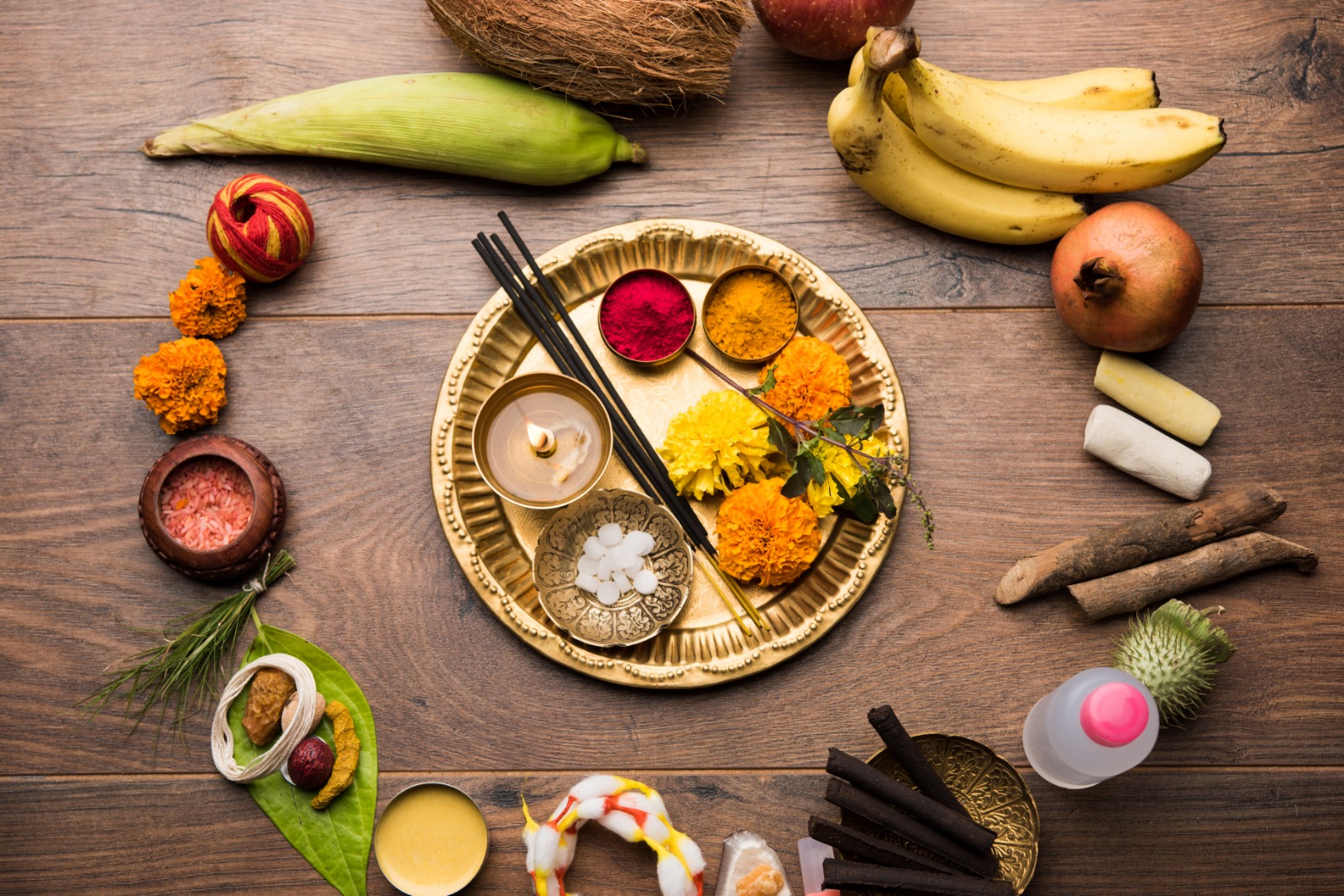 A flat lay of pooja essentials — coconut, banana, flowers, kumkum and incense